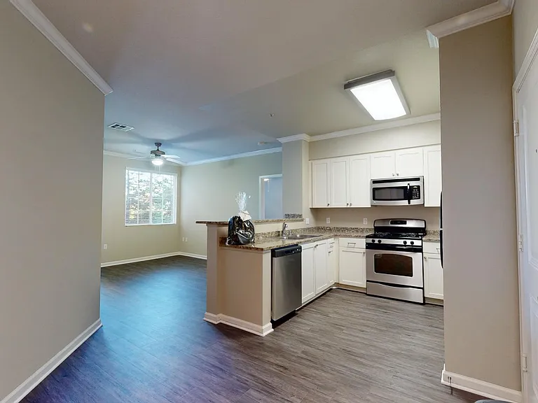 Apartment kitchen with stainless steel appliances, dining and living room with wood-style flooring.