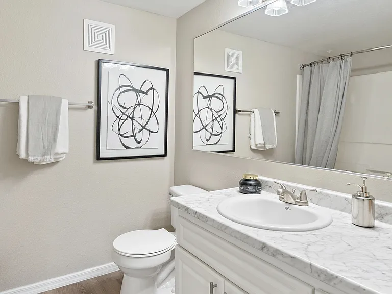 Enjoy a modern and stylish bathroom featuring a marble countertop, sleek fixtures, and a large mirror.