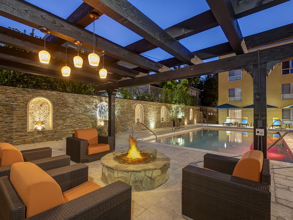 Apartments in Burbank, CA Pergola with Fire Pit and Seating Area View of Pool with Lounge Chairs Lit Up at Night.jpg