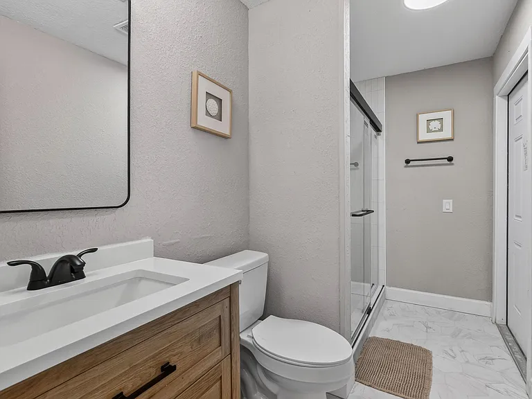 Bathroom features a single-sink vanity, framed mirror, and a shower/tub combo with sliding glass doors and tile surround.