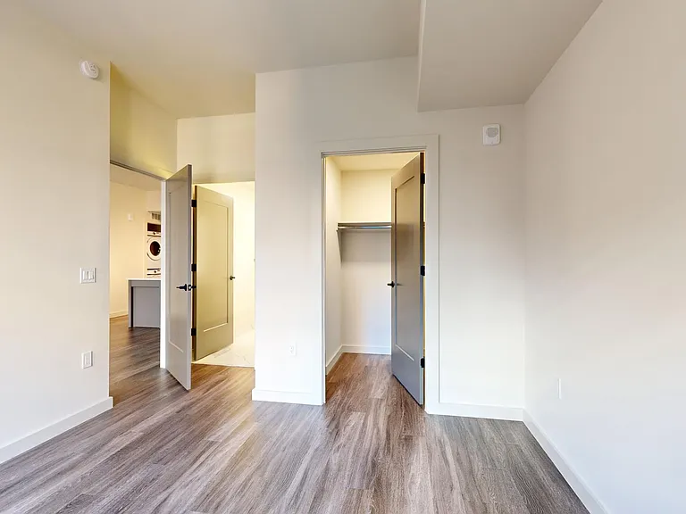 Spacious apartment bedroom with large closet, attached bathroom, and wood-style flooring.
