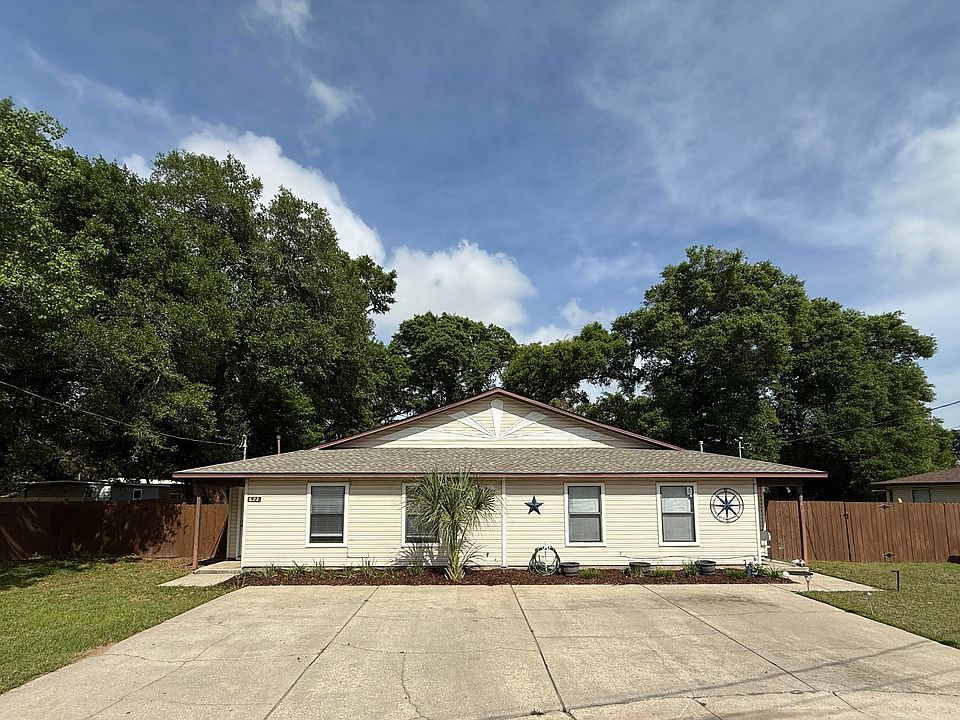 Front view of a light-colored duplex with two designated parking spaces, a fenced backyard, and a neat lawn. Ideal for comfortable, low-maintenance living.