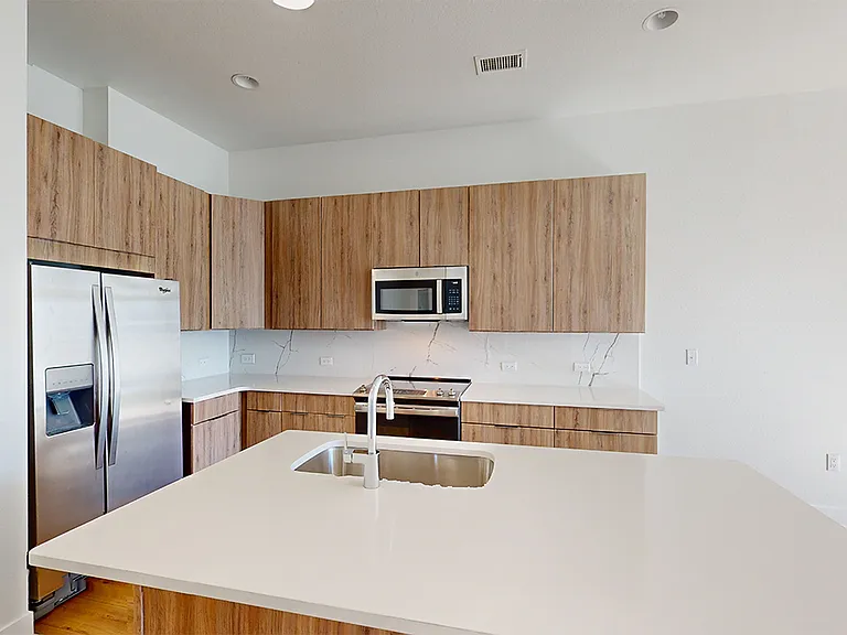 Apartment kitchen with stainless steel appliances, quartz countertops and wood-style flooring.