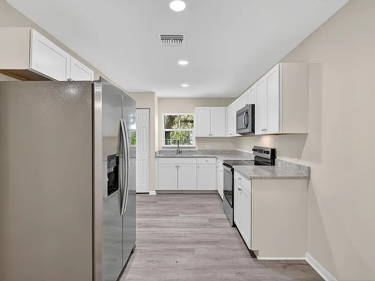 Updated galley kitchen with ample white cabinetry, granite-look counters, and stainless steel appliances plus a windowed sink