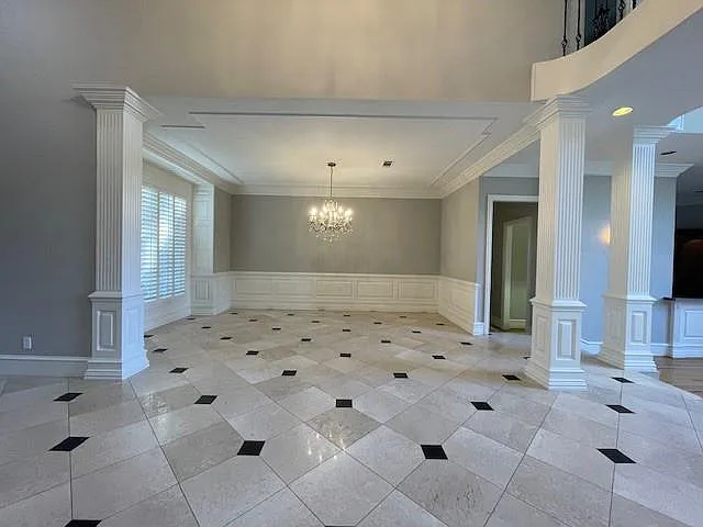 Unfurnished dining area with decorative columns, wainscoting, a chandelier, a decorative wall, and ornamental molding