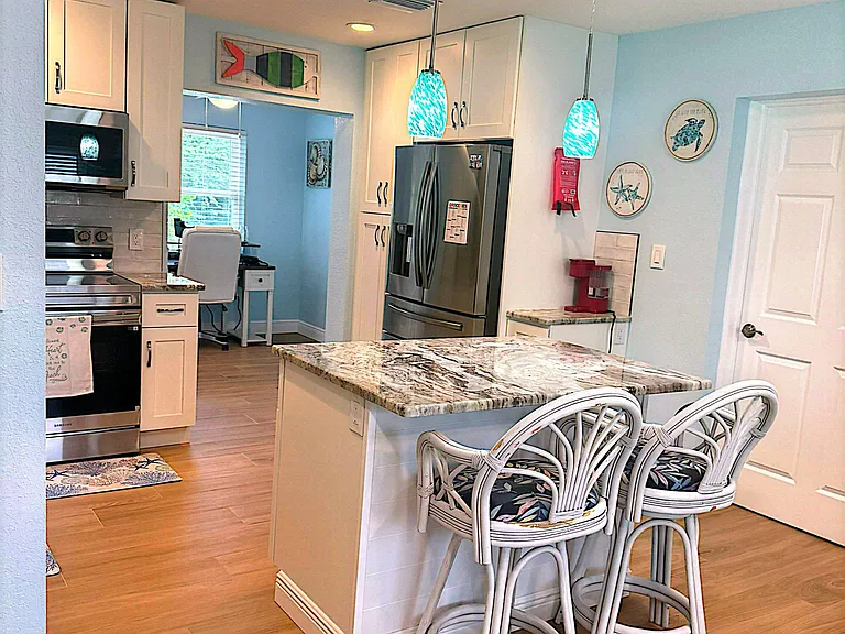 Kitchen with an island breakfast bar, pendant lighting, and stainless-steel appliances plus ample white cabinetry.