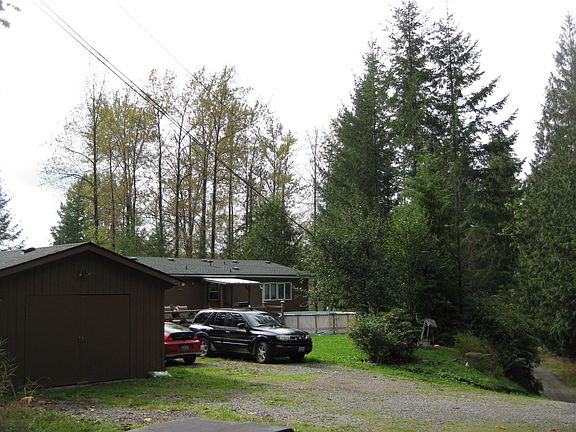View of house and garage from the north side of the gravel road. Road is also used by house at top of hill.