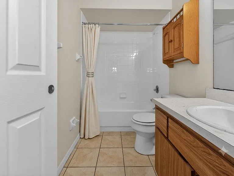 Full bathroom with tub/shower combo, tiled flooring, and a long vanity with mirror plus cabinet storage.