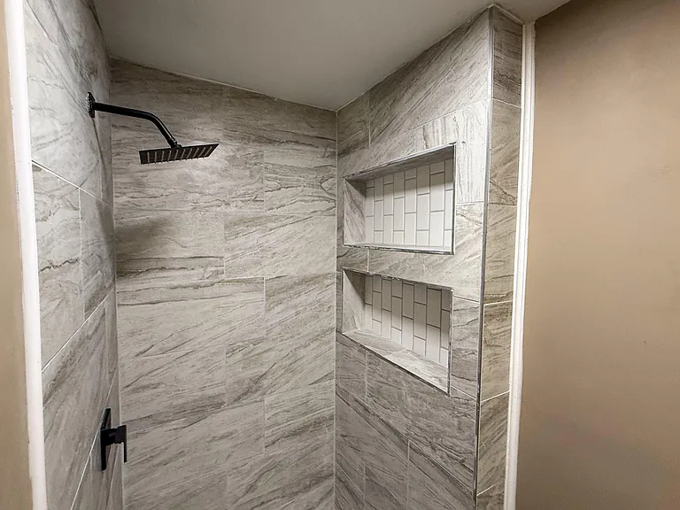 Tiled walk-in shower with a rain-style showerhead and built-in recessed shelving for toiletries and storage.