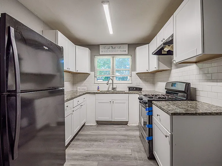 Efficient galley kitchen with white cabinetry, subway-tile backsplash, ample counters, and a window over the sink.