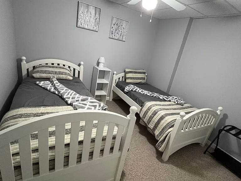 Compact bedroom set up with two twin beds, a small shelving unit, and soft carpeted flooring for easy upkeep.