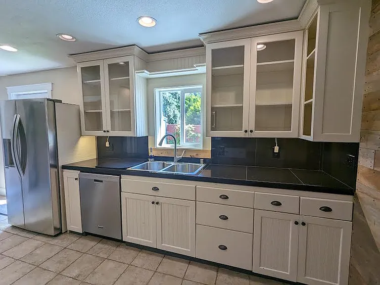 Kitchen with black granite counters, sink with window to patio, fridge and dishwasher.