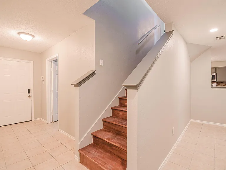 Welcoming entry area with durable tile flooring, stairway access to upper level, and sightline into the kitchen.