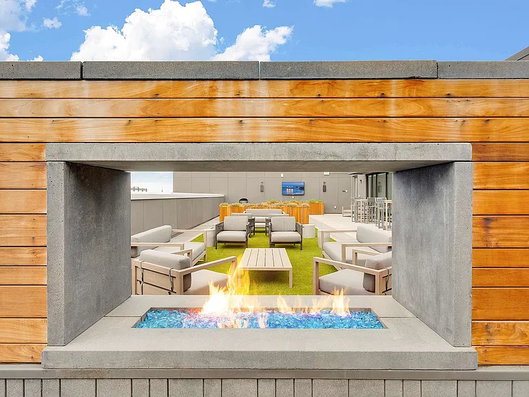 Inviting rooftop lounge featuring a modern fireplace, plush seating, and vibrant blue sky backdrop.