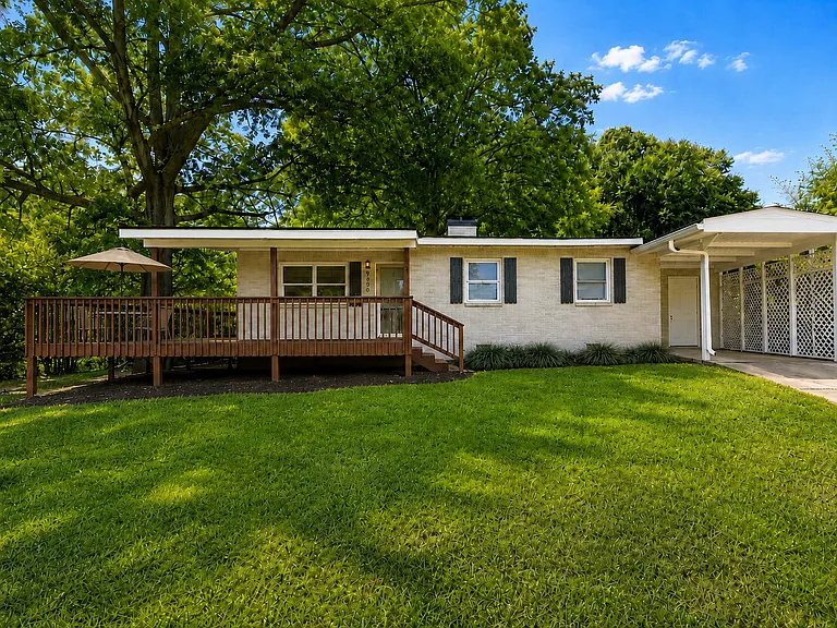 Single-story brick home with raised front deck, one-car carport and additional driveway parking.