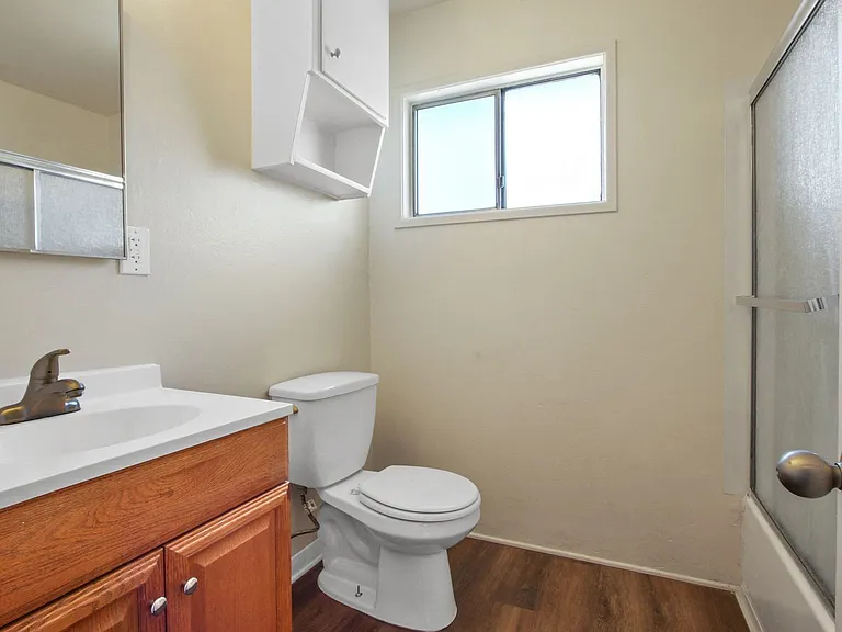 Bathroom with shower and tub combo at the right, single vanity with wood style cabinet