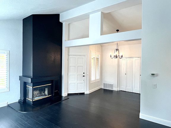 Living room overlooking cozy fireplace, main entrance, vaulted ceilings, and dining area.