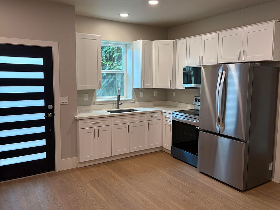 Modern kitchen with window and cabinets and stainless steel appliances like fridge, electric stove, microwave, garbage disposal