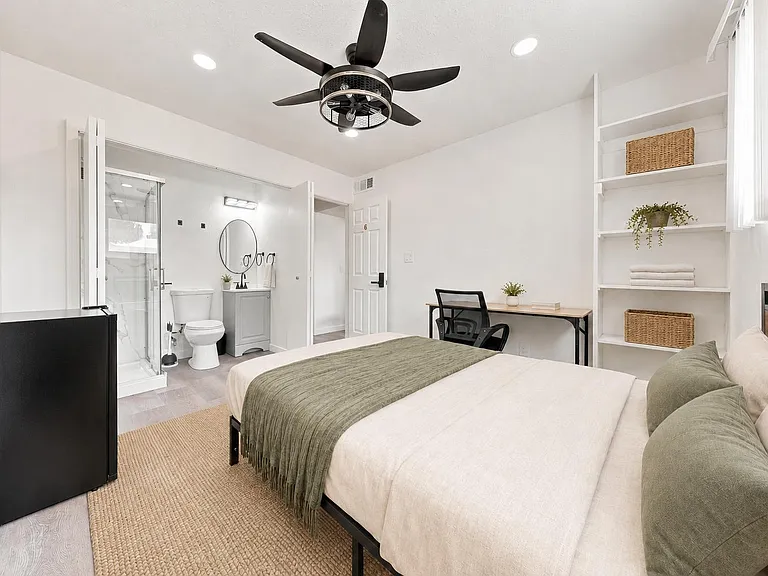 Private bedroom suite with ceiling fan, work desk, built-in shelving, and an en-suite bath with glass shower enclosure.