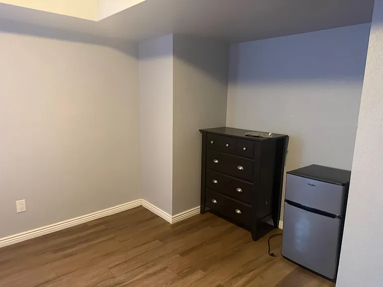 Bedroom area with durable flooring, a dresser for storage, and an in-room mini fridge for added convenience.