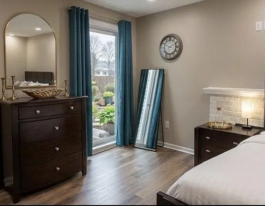 Furnished bedroom with wood-look flooring, dresser storage, full-length mirror, and patio door access to the yard.