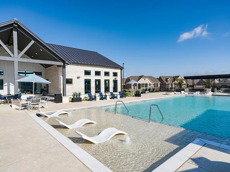 Resort-style pool with shallow lounging, shaded seating, and a modern clubhouse backdrop creates an inviting place to unwind or spend time together.