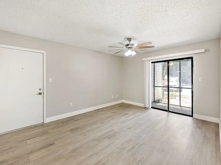 Bright and spacious living area with chic laminate flooring, a modern ceiling fan, and wide sliding glass doors leading to a serene outdoor view.