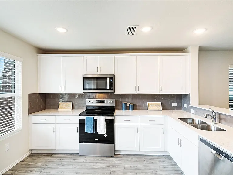 Modern kitchen featuring white cabinetry, stainless steel appliances, light-toned countertops, a dark-toned backsplash, and wood-finish flooring