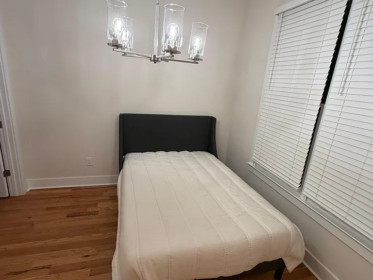 Private bedroom with hardwood floors, a large window with blinds, and an overhead light fixture for comfortable everyday livi