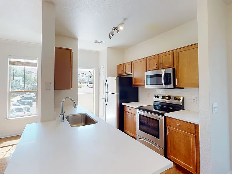 Apartment kitchen with stainless steel appliances and wood-style flooring. Quartz-style countertops (shown here) are available in select homes.