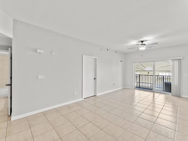 Bright and airy living space with sleek tiled flooring, modern ceiling fan, and large sliding glass doors leading to a balcony.