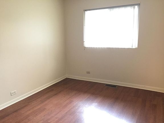 Bedroom with wood laminate flooring and vertical blinds.