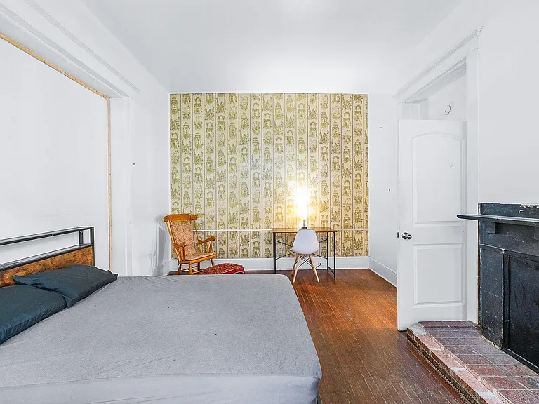 Furnished bedroom with hardwood floors, dedicated desk space, and a decorative fireplace for added character.
