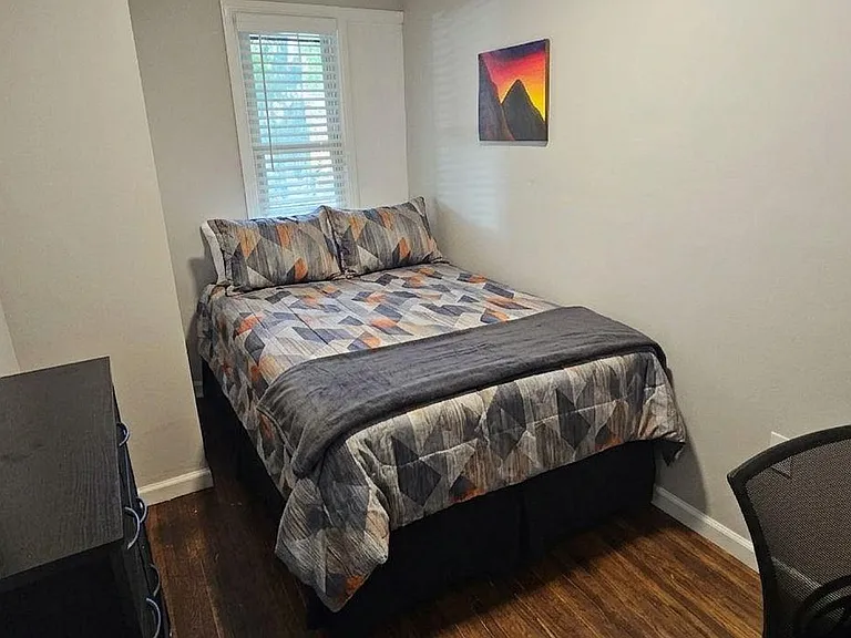 Furnished bedroom with a full-size bed, dresser storage, and a window with blinds for added privacy and daylight.