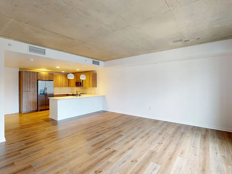 Apartment kitchen with stainless steel appliances, dining and living room with wood-style flooring.