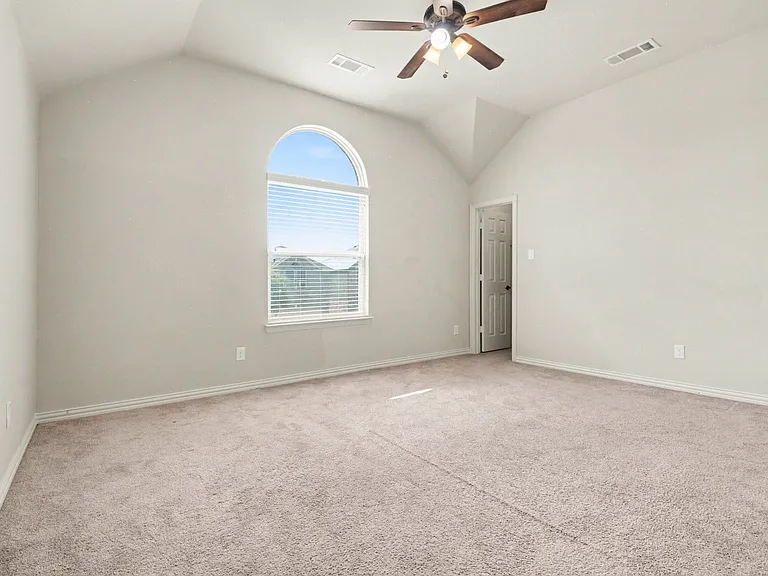 Spacious room featuring vaulted ceilings, a large arched window with blinds, a ceiling fan with integrated lighting, and neutral tone carpeting