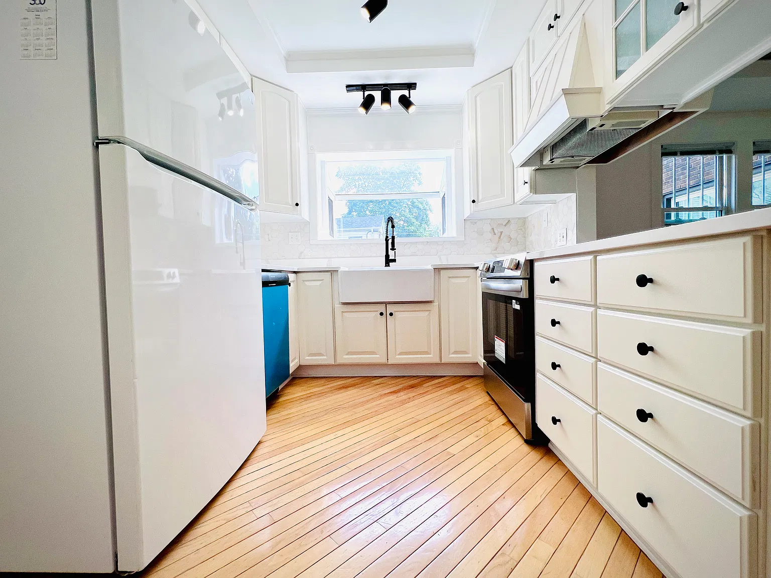 Newly updated kitchen featuring sleek quartz countertops, a classic white farmhouse sink with a high-arc gooseneck faucet, and brand-new electric appliances including an oven and dishwasher.