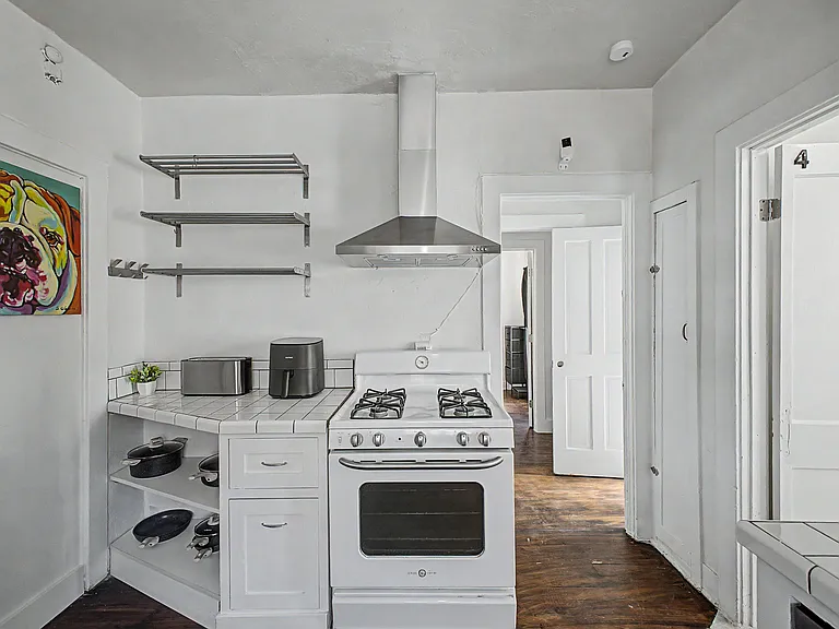 Functional kitchen area with gas range and vent hood, tiled counters, and open shelving for easy everyday storage.