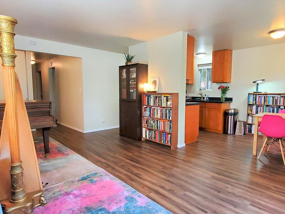 View of Living Room, Dining area, Kitchen, Hallway to bath and 2 bedrooms. There are 3 large windows in living room and dining area. 2 entry doors - 1 on left by grand piano and 1 on right next to dining area.