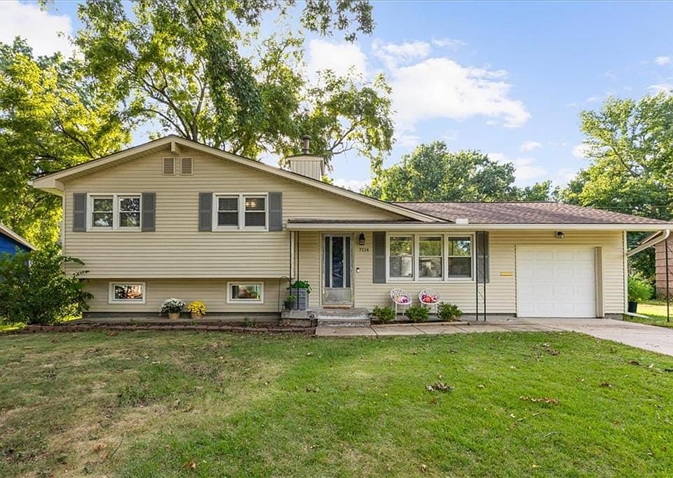 Mature trees frame a classic split-level exterior featuring neutral siding and an attached garage.