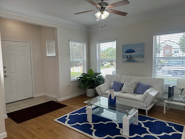 Bright and inviting living room with a stylish white sofa, blue-themed decor, glass coffee table, and natural light streaming through large windows. Bright and inviting living room with a stylish white sofa, blue-themed decor, glass coffee table, and natu