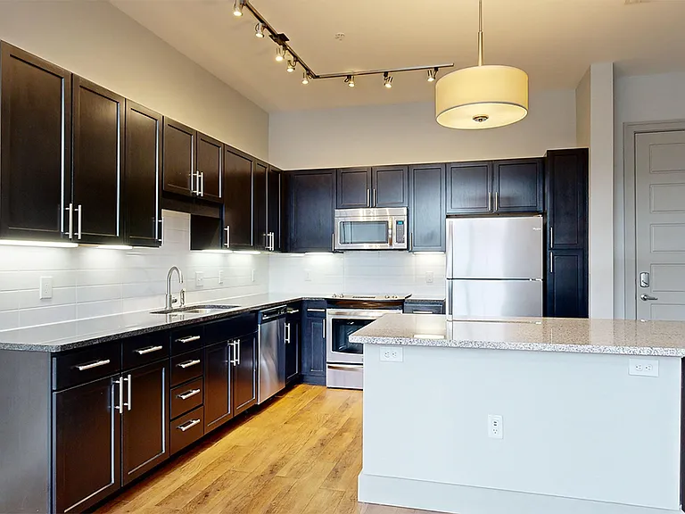 Apartment kitchen with stainless steel appliances, granite countertops and wood-style flooring.