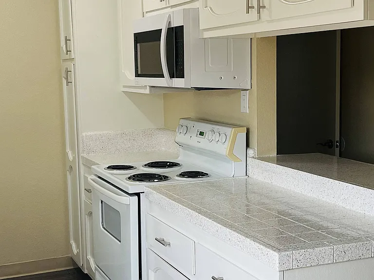 Kitchen with white cabinets and appliances, plank style flooring, and server bar at Plaza Verde Apartments in Escondido, California.