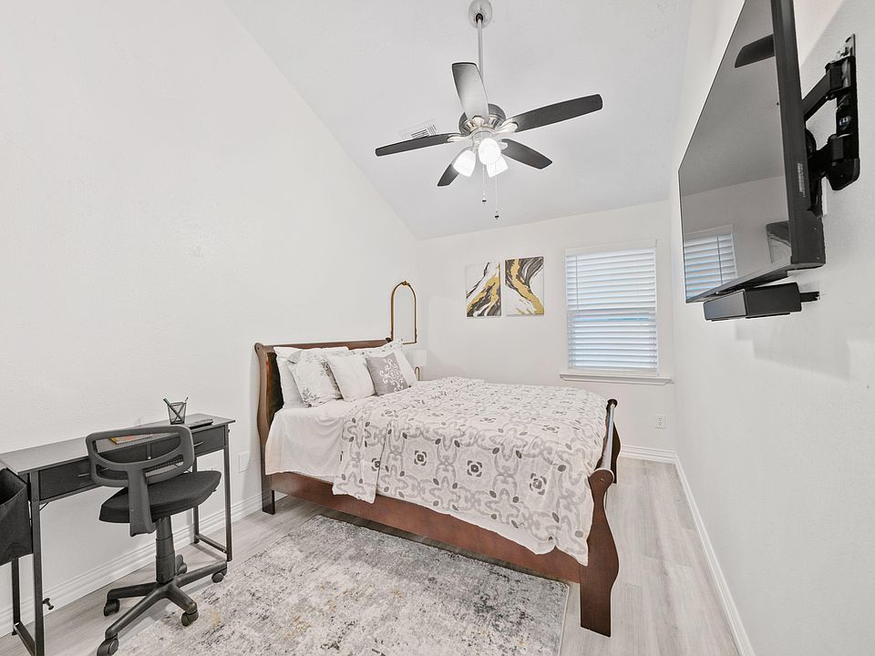 Furnished bedroom with a full bed, work desk, ceiling fan, and wall-mounted TV, plus a window with blinds for privacy.