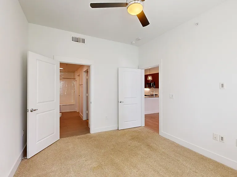 Spacious apartment bedroom with large closet, attached bathroom, and plush carpet flooring.