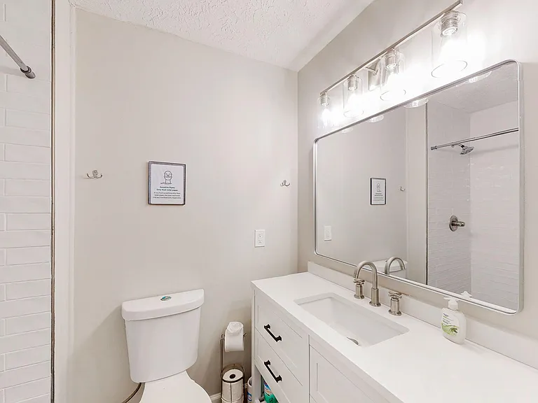 Updated full bath with a wide vanity, large mirror, and ample under-sink storage, plus a tub/shower with tile surround.