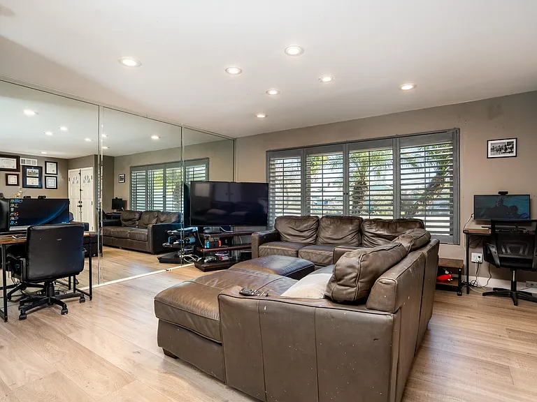 Living room has large window with shutters over looking front yard. Walled mirrors.