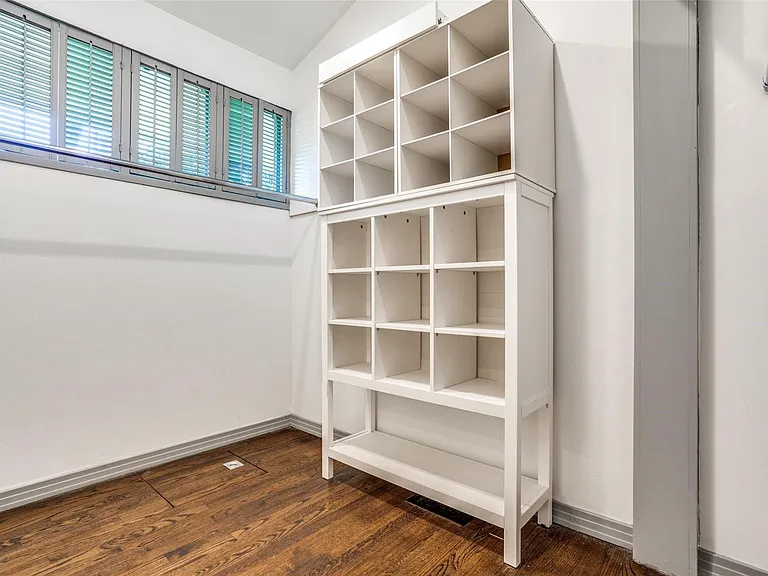 Closet space featuring wood-finish flooring, white walls, and a multi-compartment shelving unit