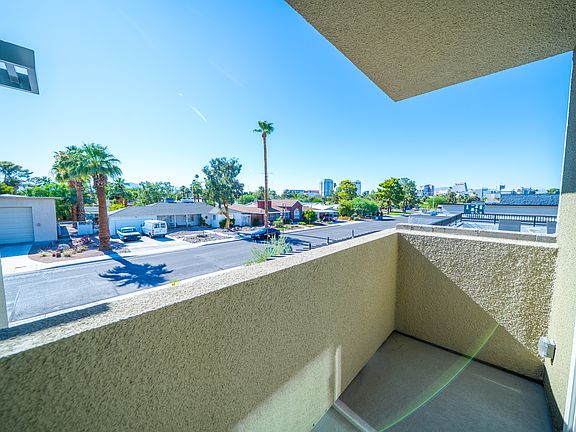 This image captures a bright balcony view overlooking a neighborhood, highlighting palm trees and the distant skyline, ideal for enjoying fresh air.