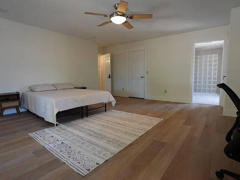 Spacious bedroom with wood-style flooring, ceiling fan, bedside table, and direct access to an adjacent bath area.